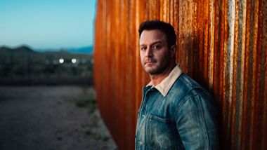 Easton Corbin leaned up again an industrial wall outside